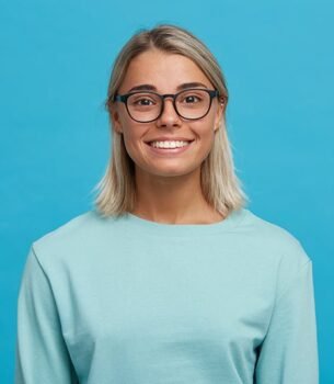 Smiling woman with blonde hair and black-framed glasses against a blue backdrop.