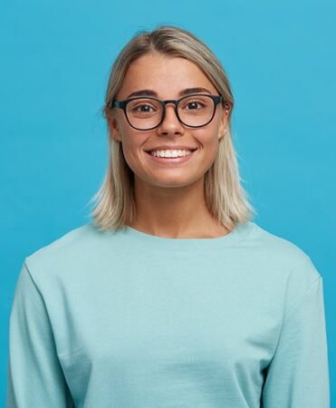 Smiling woman with blonde hair and black-framed glasses against a blue backdrop.
