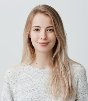 Portrait of a smiling woman with long blonde hair in a light gray sweater against a pale backdrop.