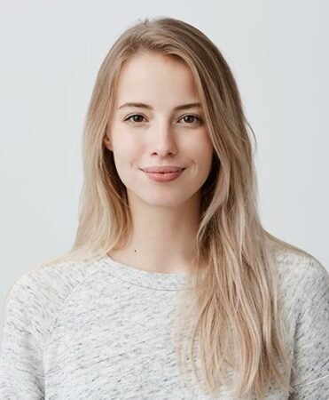 find more africa #findmoreafrica › Portrait of a smiling woman with long blonde hair in a light gray sweater against a pale backdrop.
