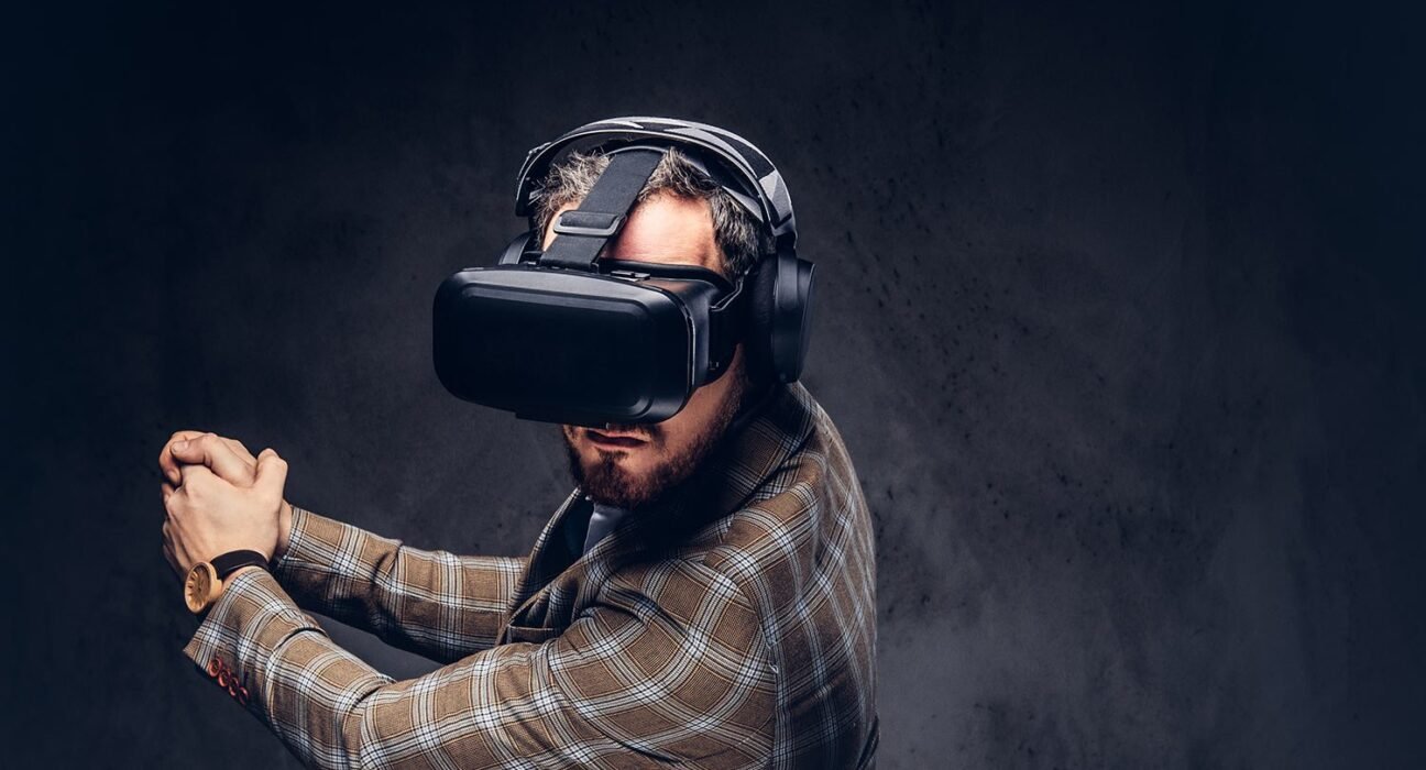 Man in a plaid blazer wearing a virtual reality headset and over-ear headphones, arms raised in a ready pose to explore VR.