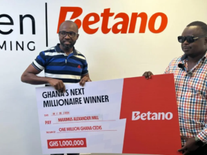 Two men pose with a large Betano prize check that reads 'Ghana's Next Millionaire Winner' and shows the amount 'GHS 1,000,000' with the Betano logo in the background.
