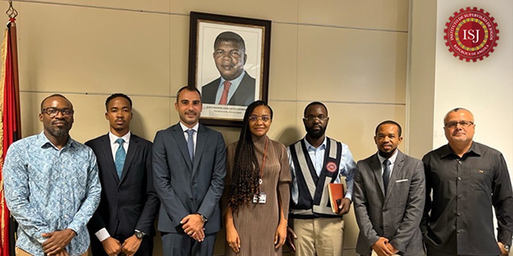 Seven professionals in business attire stand in a row in a conference room, with a framed portrait and an ISJ emblem in the background.