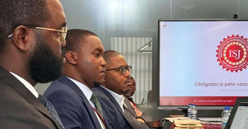 Four men in suits seated at a conference table, watching a presentation on a screen displaying the ISI logo and Portuguese text.