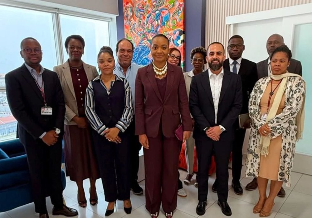 find more africa #findmoreafrica › Group of ten professionals in business attire posing for a photo in a modern office with a colorful abstract painting behind them.