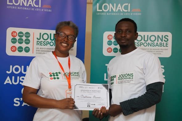 find more africa #findmoreafrica › Two event participants in white 'Jouons Responsable' shirts hold a certificate between them, standing in front of blue and green banners.