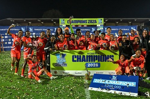 Women’s football team in red uniforms celebrates on a night field with Champions 2026 banners and a large $200,000 prize check.