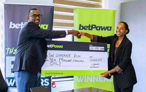 Two professionals shake hands while presenting a large mock cheque for ten million shillings to The Corporate Run, with BetPawa banners in the background.