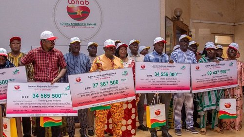 Group of people on a stage holding oversized ceremonial checks at a lottery prize event.
