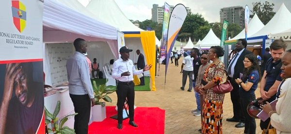 Officials discuss at an outdoor expo with white tents and colorful booths; banner reads National Lotteries and Gaming Regulatory Board.