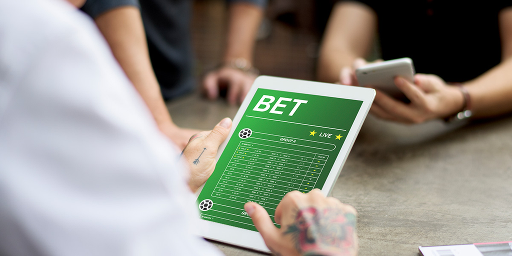Person using a tablet that displays a green betting interface with the word BET on screen.